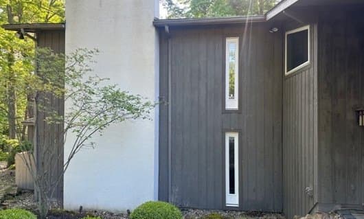Tall side wall of dark weathered wood siding beside a white stucco section, before