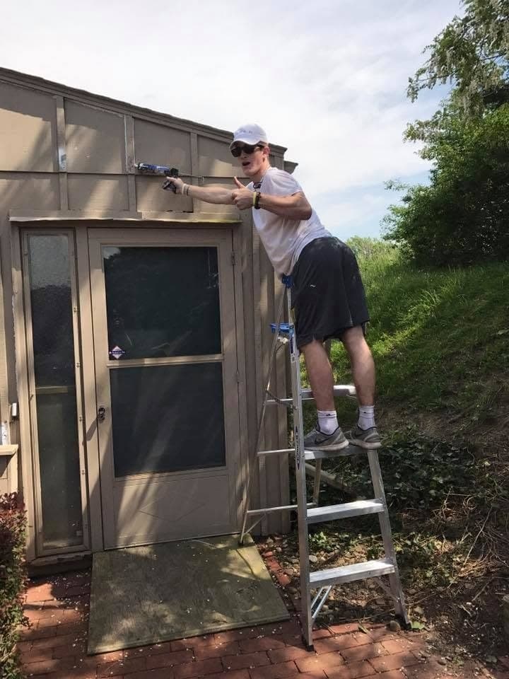 Early Wildwood painter on a step ladder giving a thumbs up beside a garage door