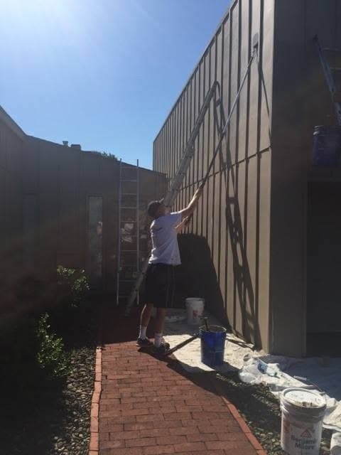 Painter brushing tall siding beside a brick walkway