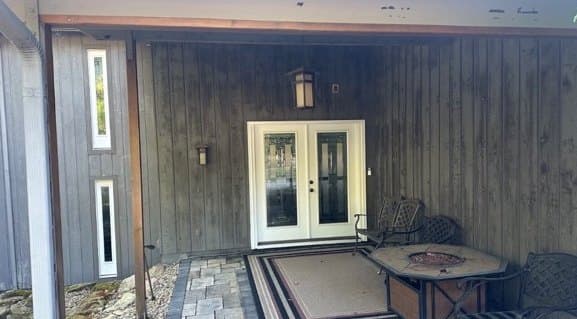 Covered entry with dark, weathered vertical wood siding before refinishing