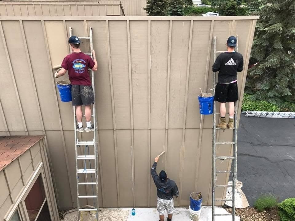 Painters on two ladders brushing tall board-and-batten siding